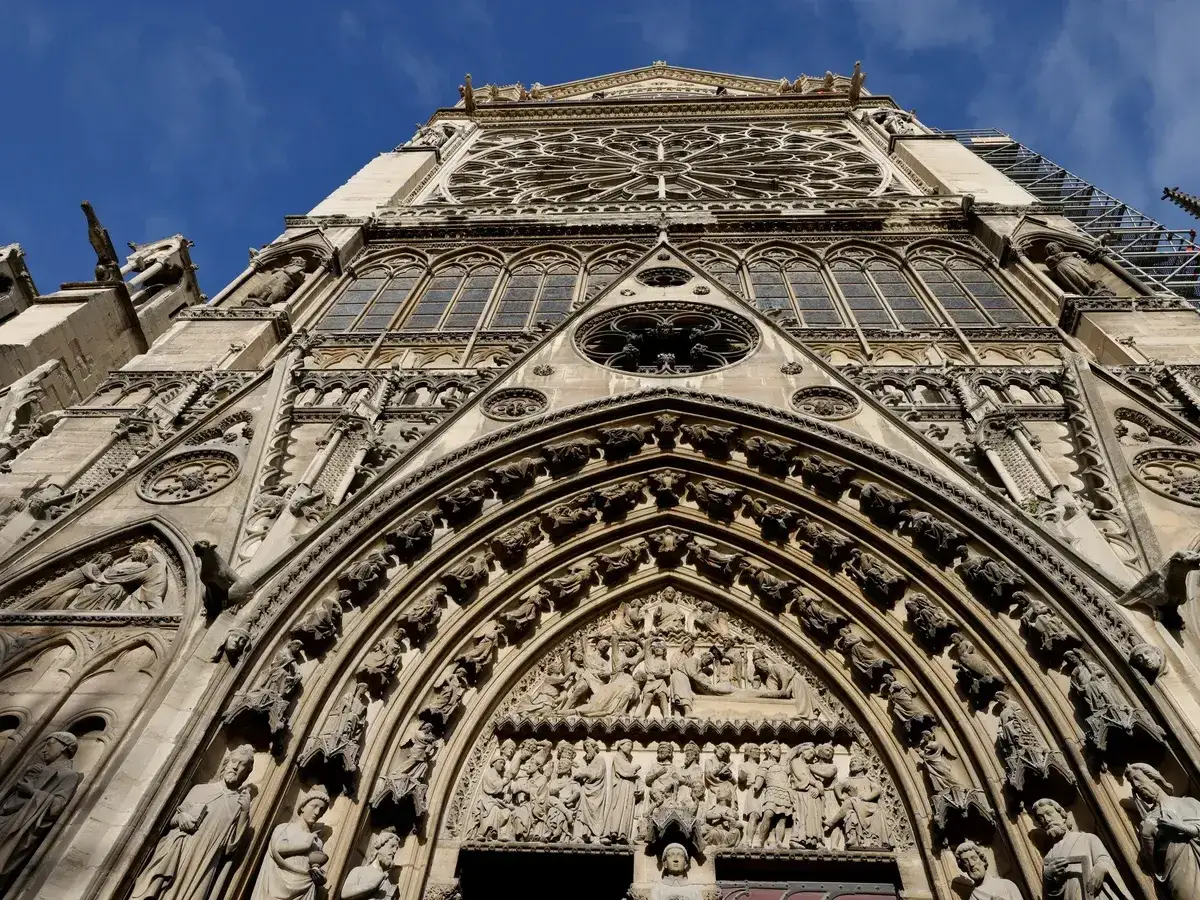 Detalle de la entrada Notre Dame, con sus intrincadas esculturas y un rosetón gótico bajo un cielo azul.
