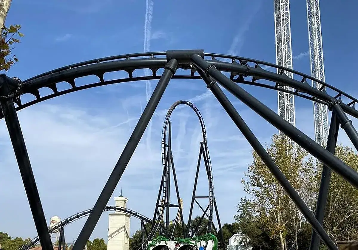 Montaña rusa oscura con bucles, torres de caída libre y arquitectura que evoca a Gotham City, Warner Bros. Park.