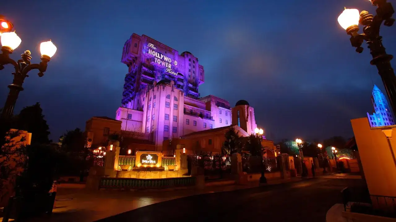 La Hollywood Tower Hotel de Disneyland Paris se ilumina de p&uacute;rpura bajo el cielo nocturno, invitando a la aventura.