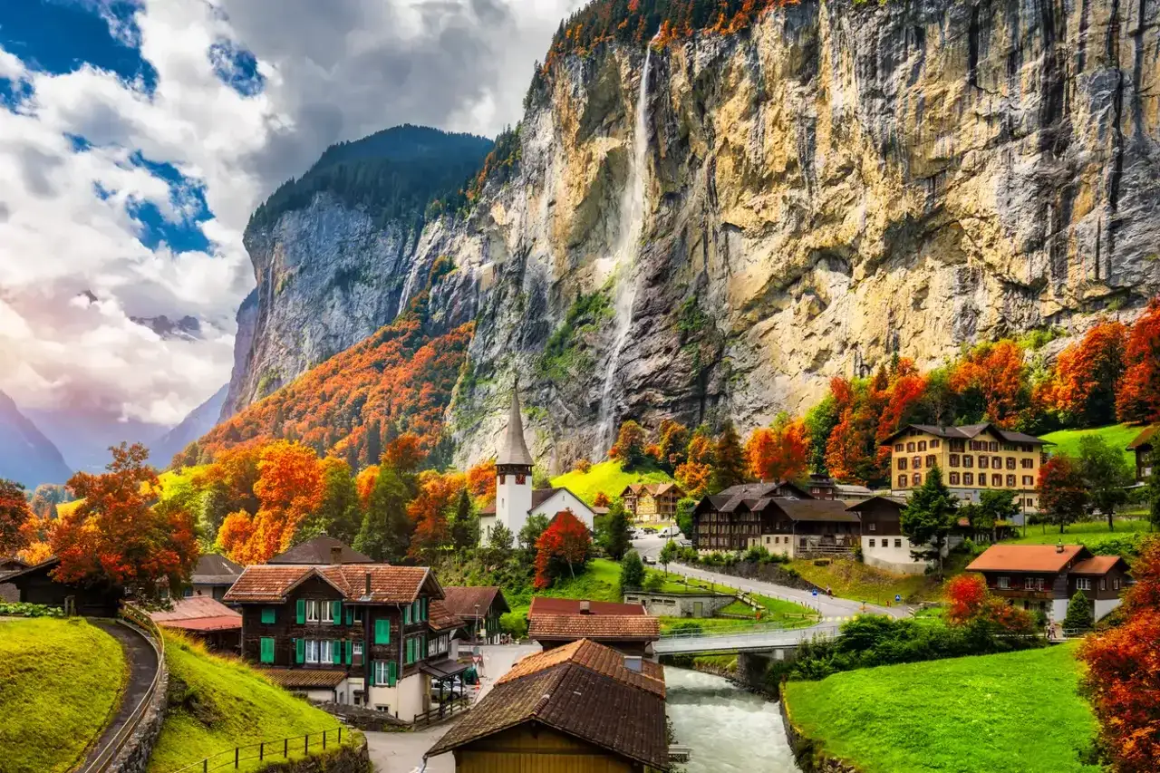 Un pintoresco pueblo suizo que ver en oto&ntilde;o, con casas de madera, una iglesia y cascadas cayendo por acantilados imponentes.