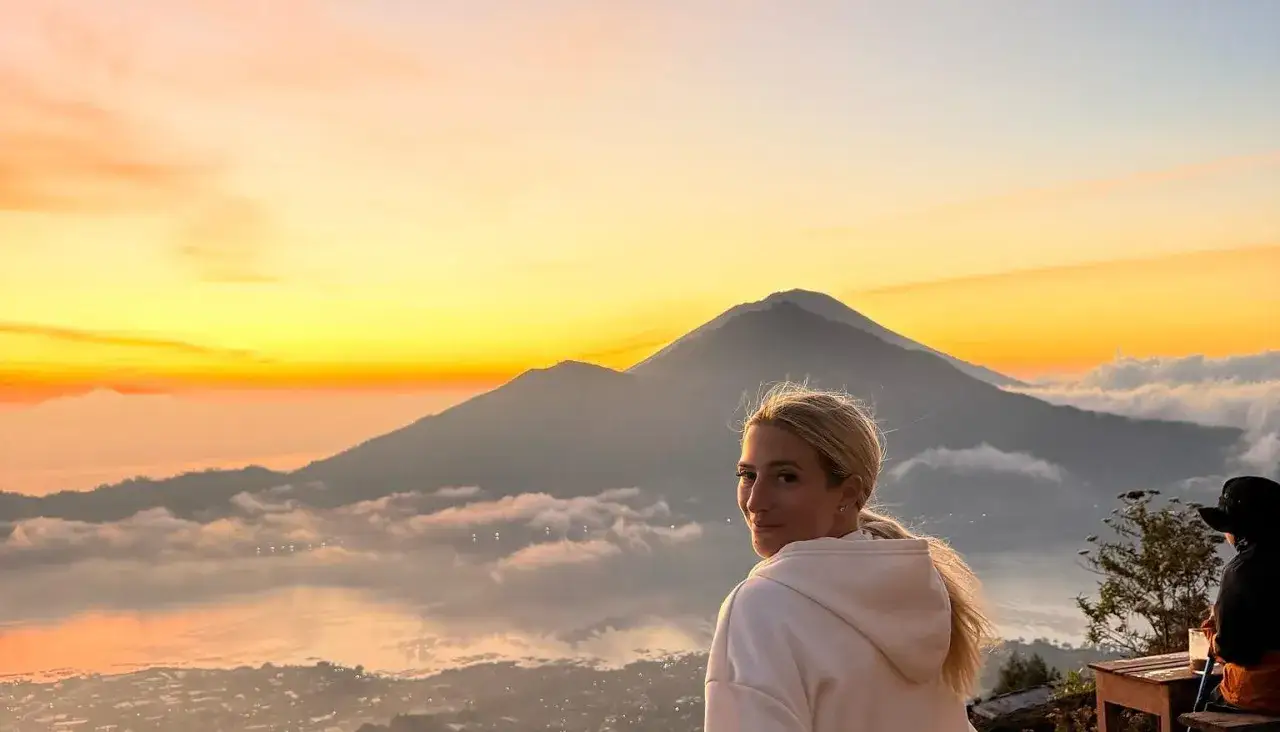 Mujer rubia disfruta un amanecer espectacular en su viaje a Indonesia 15 d&iacute;as. Monta&ntilde;as y nubes cubren el paisaje.