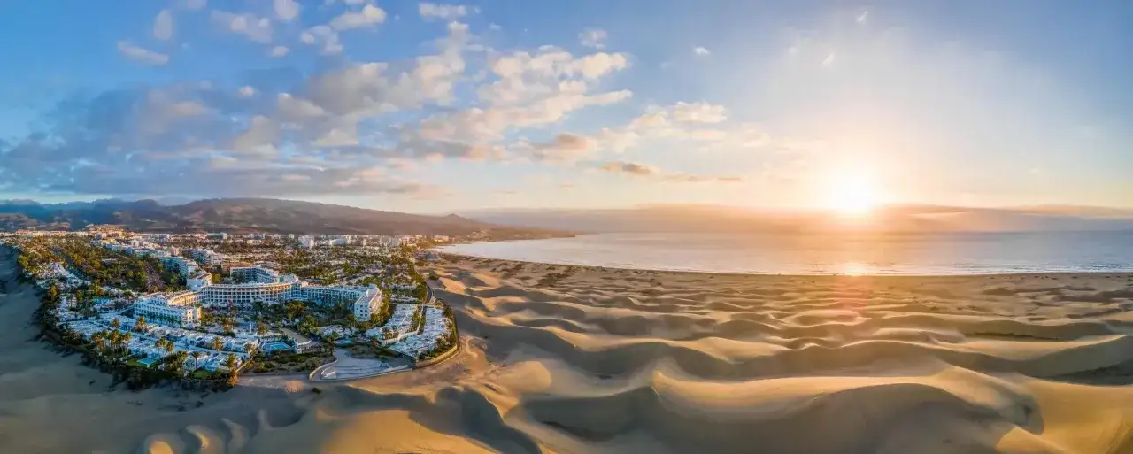 Dunas doradas y resorts blancos junto al mar, un paisaje idílico de las mejores playas de Gran Canaria al atardecer.