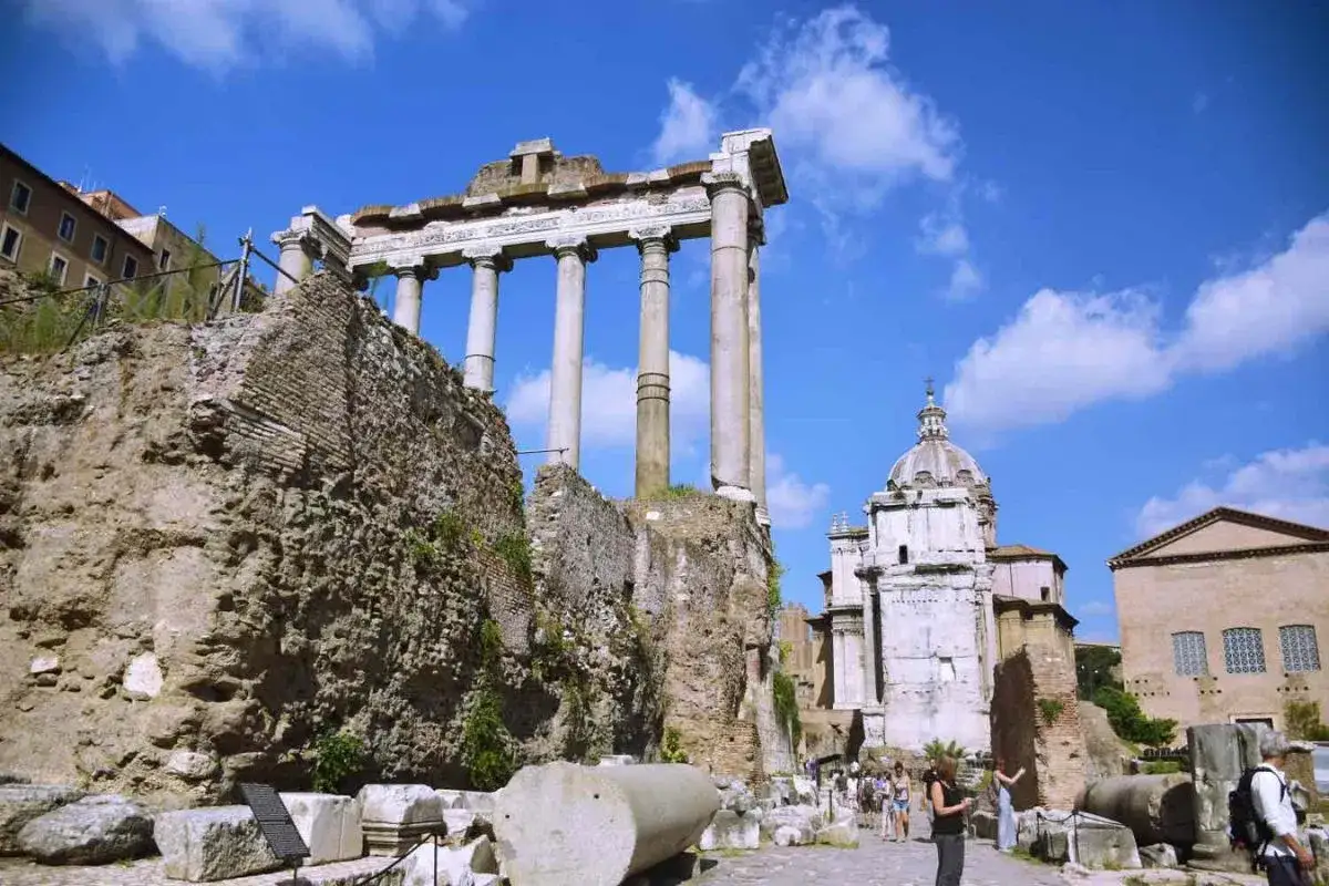Ruinas del Foro Romano, un lugar imprescindible que ver en Roma en 4 días. Columnas antiguas y cúpula de iglesia bajo un cielo azul.