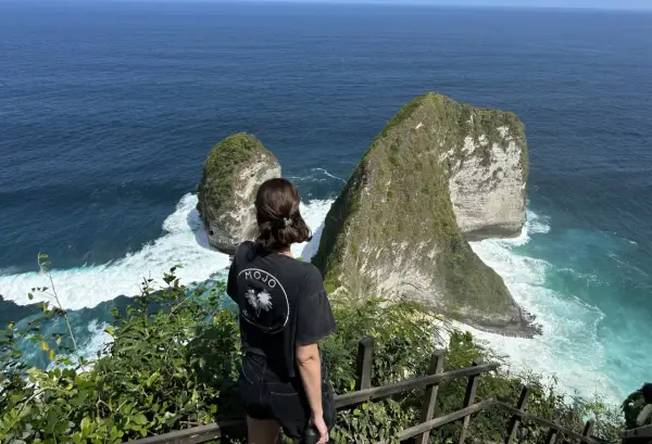 Una mujer admira el paisaje de acantilados verdes y mar turquesa, un momento de su viaje a Indonesia de 15 días.