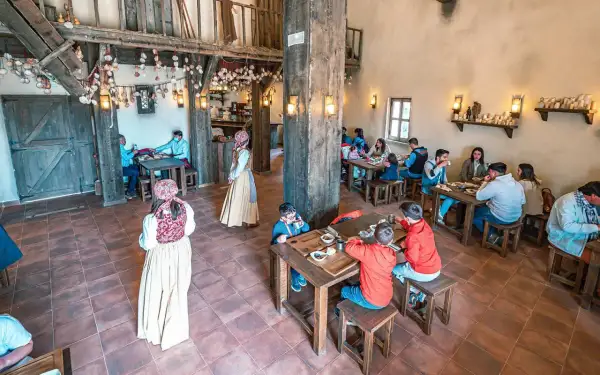 Ambiente rústico para comer en Puy du Fou. Familias y parejas disfrutan de una comida en un comedor de madera con decoración temática.
