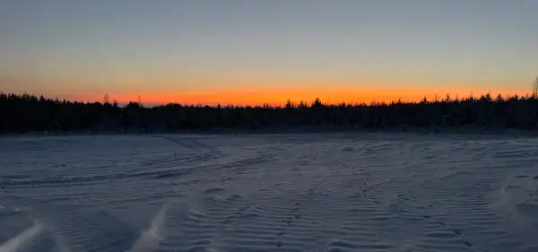 Paisaje invernal con cielo anaranjado al atardecer. Huellas en la nieve sugieren el camino para saber como ir a Laponia.