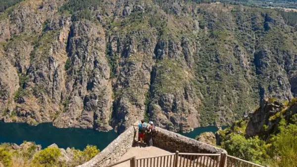 Dos excursionistas contemplan un cañón con un río azul, ideal para rutas por Galicia.