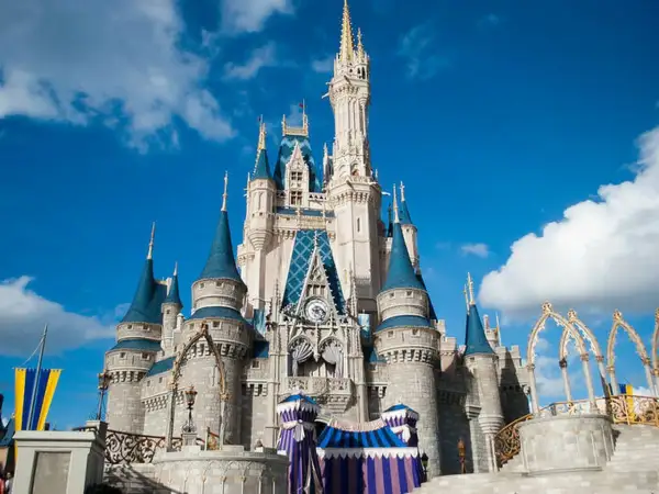 El icónico castillo de Disneyland se alza majestuoso bajo un cielo azul con nubes blancas, invitando a la magia.