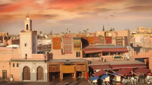 Mercado marroquí con alfombras coloridas colgadas, un minarete y tejados rojos. Consejos para viajar a Marruecos.