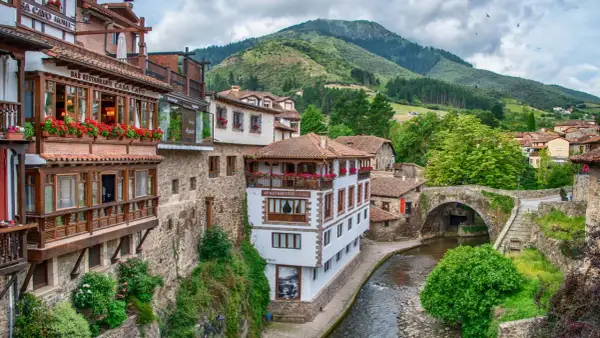 Encantadores pueblos costeros de Cantabria con casas de madera y piedra, balcones floridos y un río serpenteante bajo un puente antiguo.