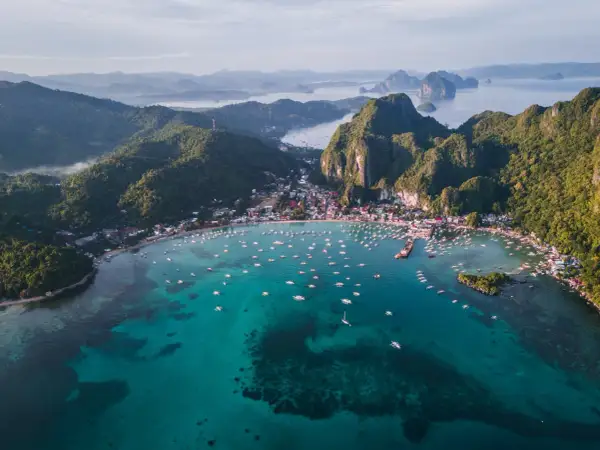 Vista aérea de El Nido, Filipinas. Un mar turquesa lleno de barcos, con una costa verde y montañosa. ¡Perfecto para tu próxima aventura con una tarjeta SIM Filipinas!