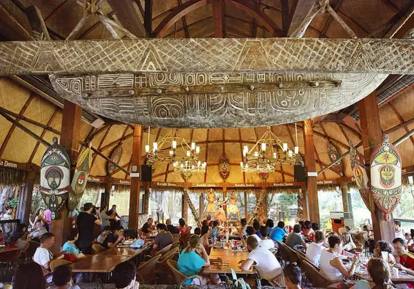 Comedor temático con decoración polinesia, similar a Bora Bora, en PortAventura. Gente disfrutando de un espectáculo.