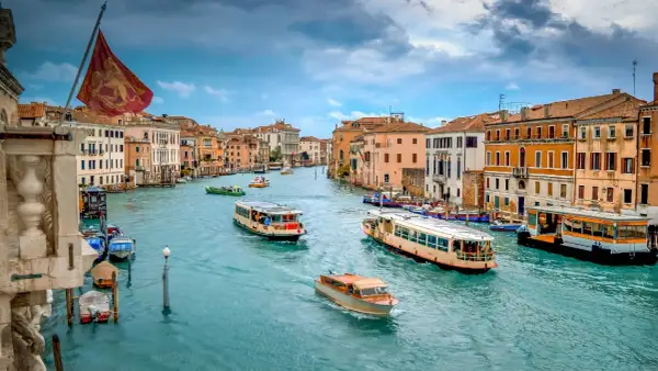 El Gran Canal de Venecia, con barcos y vaporetos, muestra cómo moverse por Venecia. Edificios coloridos flanquean el agua turquesa.