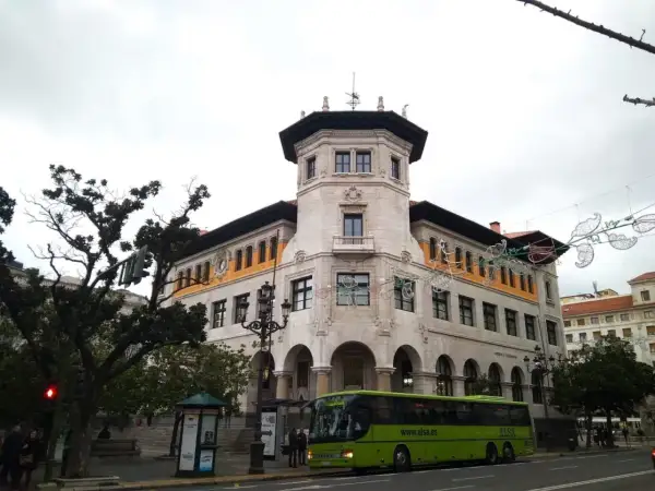 Autobús verde de ALSA en la calle, frente a un edificio histórico. Un buen lugar para aparcar en Santander y disfrutar de la arquitectura.