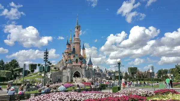 El castillo rosa de Disneyland Paris, rodeado de flores y gente, es el centro de sus atracciones.