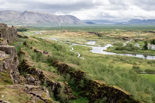 Paisaje de Thingvellir National Park con un río serpenteante, montañas al fondo y una grieta rocosa en primer plano.