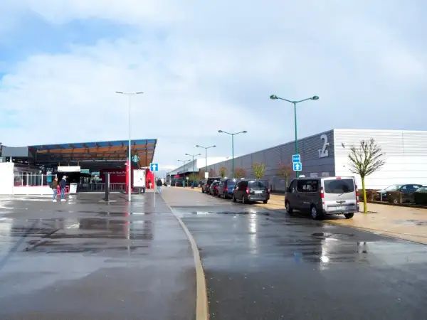 Llegando a **París Beauvais al centro**, taxis esperan bajo un cielo nublado. El aeropuerto tiene una zona de embarque y un edificio largo con el número 2.
