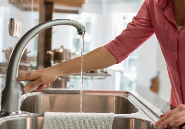 Mano abre grifo en cocina. El agua fluye, demostrando que el agua de París es potable y segura para beber.