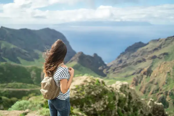 Mujer con mochila admira el paisaje montañoso y el mar, imaginando el viaje en barco Tenerife La Gomera.